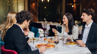 Şık masa düzeni, sıcak ışıklar ve özenli yemek sunumuyla hem lezzeti hem atmosferi hissettiren davetkar bir restoran ortamı.